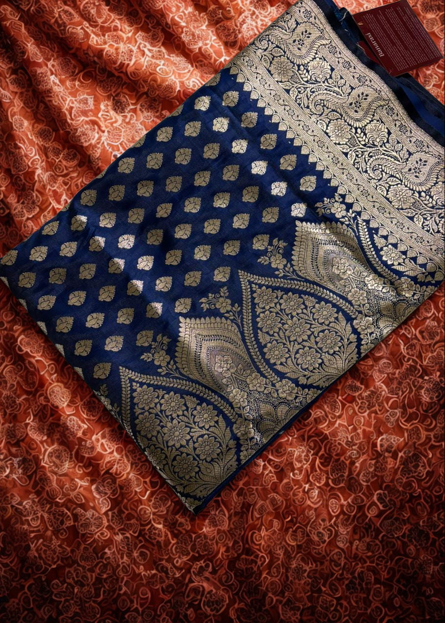 Beautiful Navy blue banarasi Silk Saree with golden zari work placed folded over a coral red color fabric 