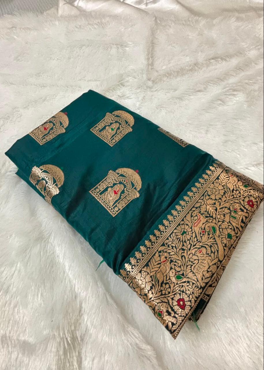 A folded teal-green Baluchari saree fabric with gold zari embroidery, featuring elephant motifs and a detailed floral border, displayed on a white faux fur surface.
