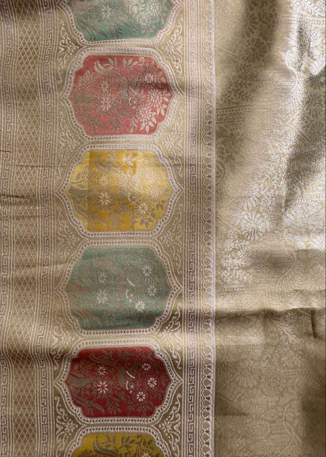 A close-up of the border of a Banarasi Silk Sareea featuring vertical bands of repeating Hexagonal motifs in muted red, yellow, and sage green, bordered by ornate beige geometric patterns.