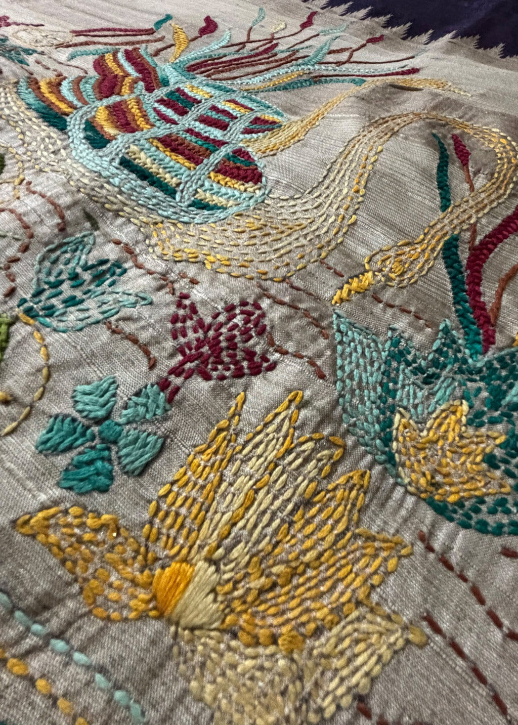 Close-up of two hand-embroidered Kantha swans in a lotus pond on beige saree pallu