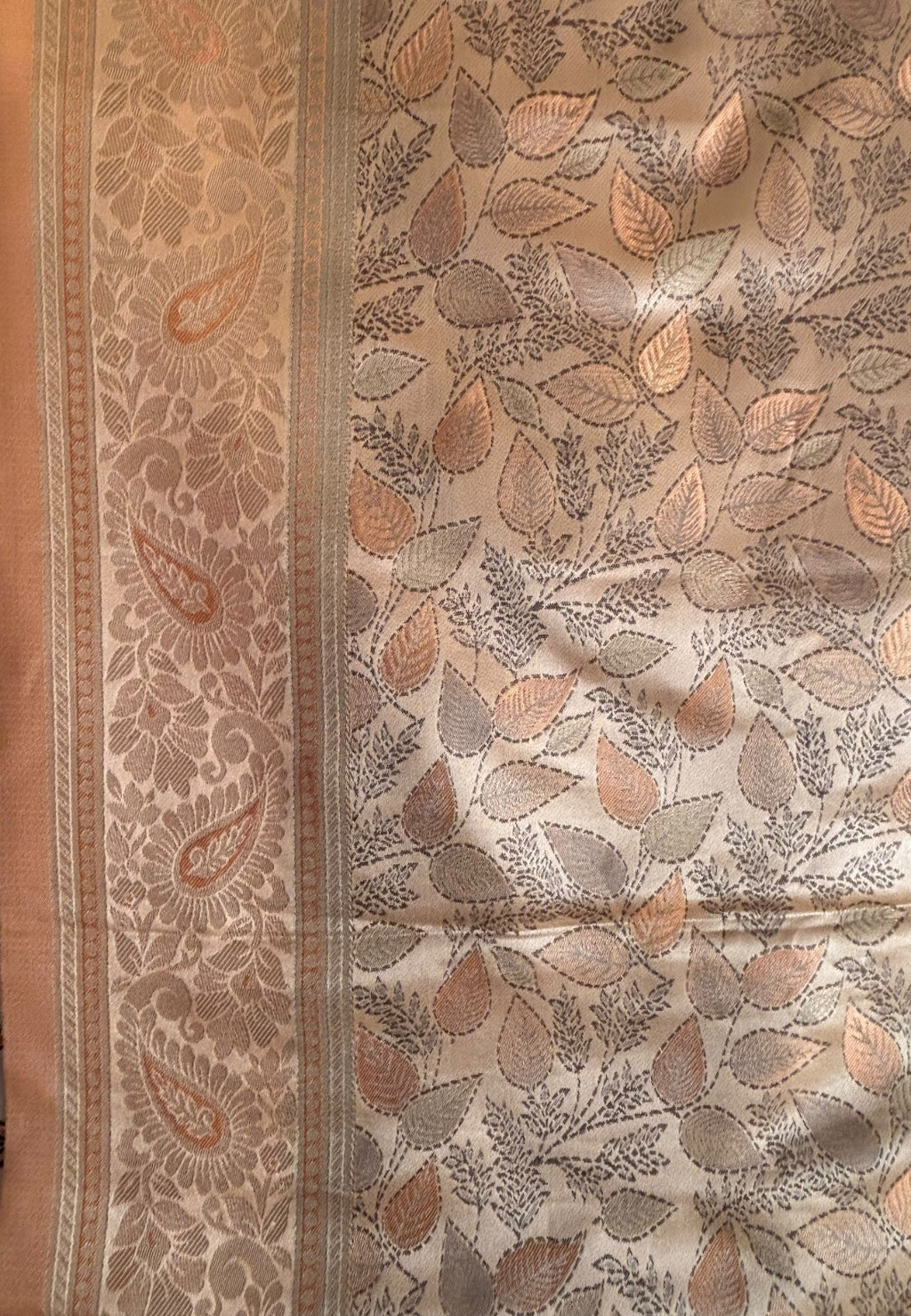 A close-up of a beige and brown paisley border and an allover leaf pattern in taupe, gray, and muted orange copper coloured Banarasi Saree