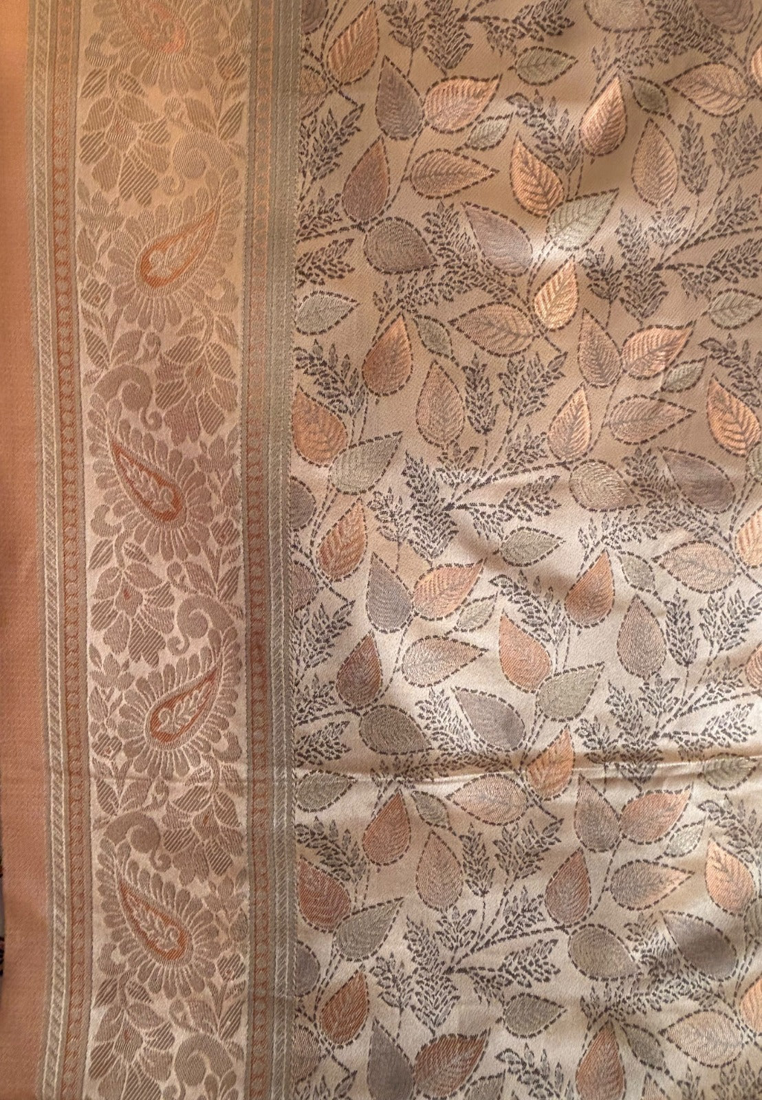 A close-up of a beige and brown paisley border and an allover leaf pattern in taupe, gray, and muted orange copper coloured Banarasi Saree
