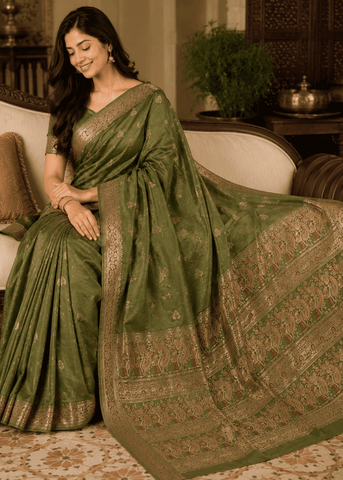Full-length view of a woman wearing an imperial moss green Baluchari silk saree with delicate gold small buti motifs, a rich gold border, and a lavishly woven pallu depicting classic mythological figures and intricate royal patterns