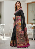 Woman wearing a black saree with colorful patterns in an indoor setting