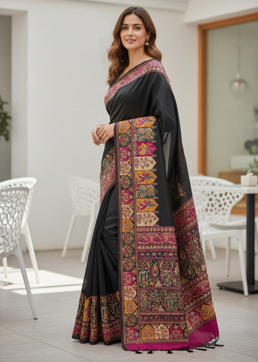 Woman wearing a black saree with colorful patterns in an indoor setting