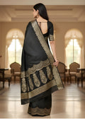 A woman wearing a black Banarasi saree with gold embroidery in an elegant indoor setting.