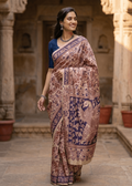 A smiling woman  showcasing the Mayur premium cotton Kalamkari saree with an intricate cream and rust floral body and a bold indigo blue peacock pallu