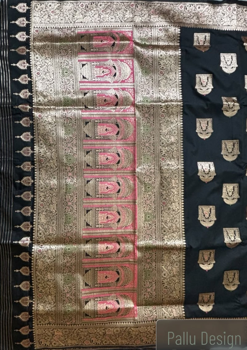 A close-up of a black and gold Baluchari silk saree with intricate zari embroidery, featuring a central pink and gold arch motif and a black border with gold motifs.