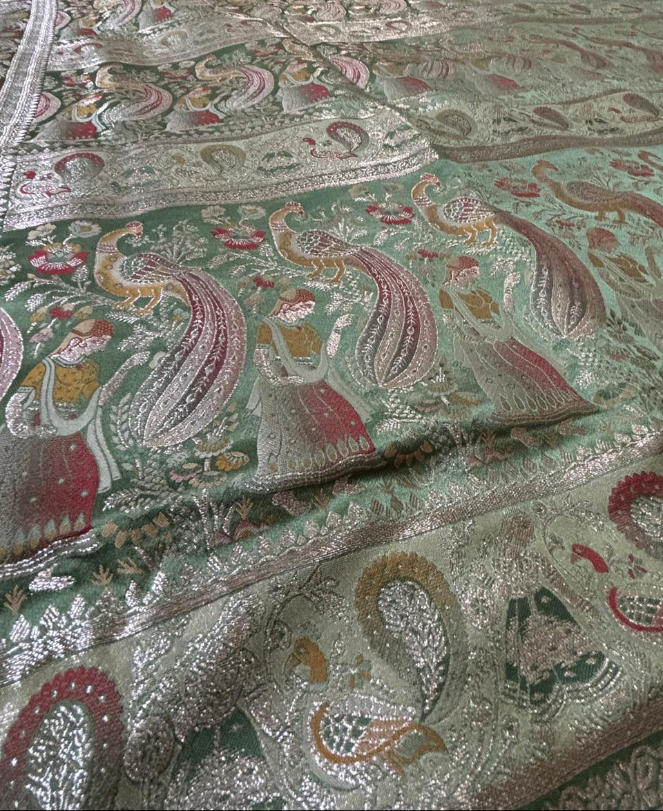 view of a  imperial moss green Baluchari silk saree with delicate gold small buti motifs, a rich gold border, and a lavishly woven pallu depicting classic mythological figures and intricate royal patterns