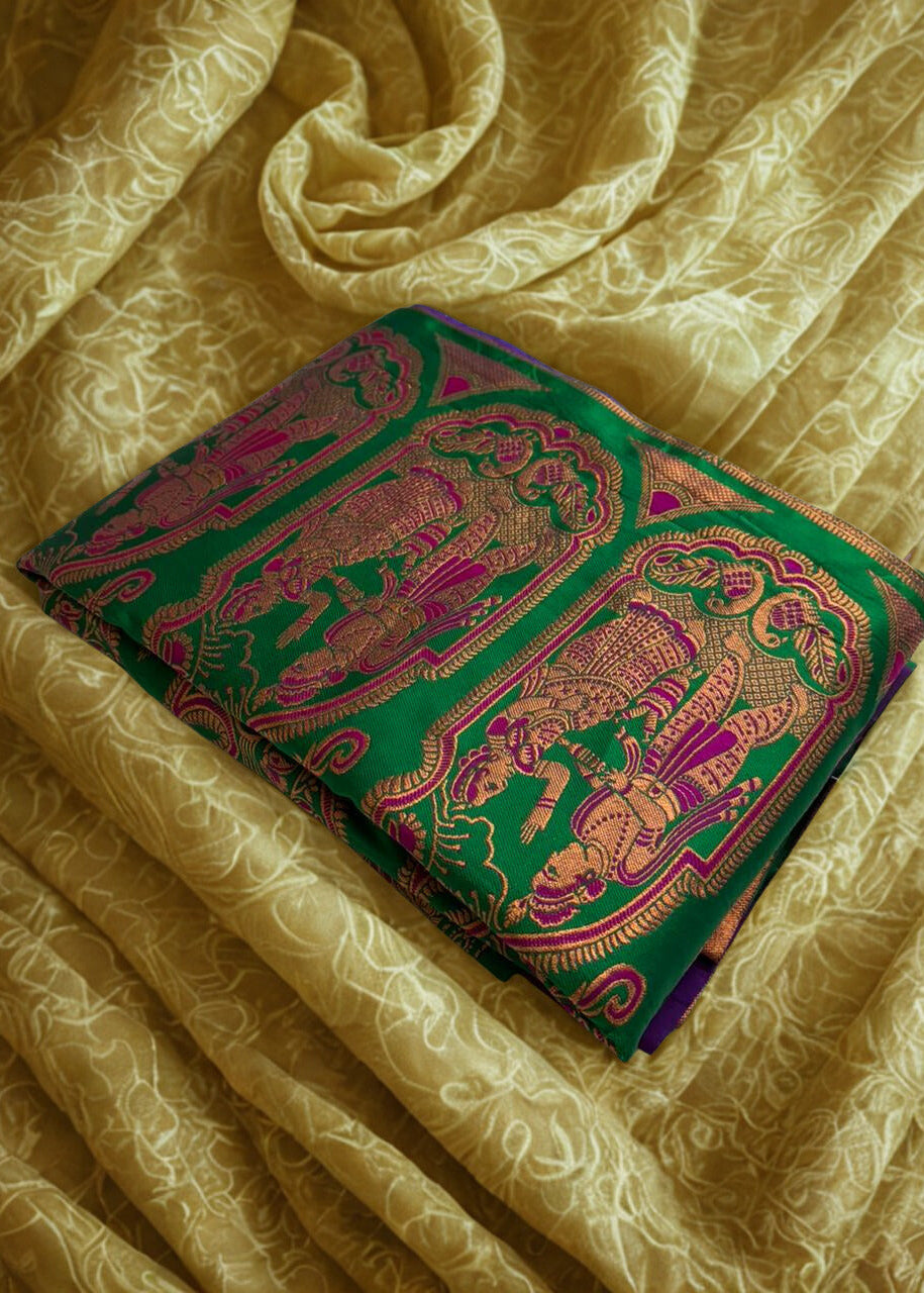 Rajrangini Baluchari silk saree in royal purple and green with intricate golden zari storytelling motifs, traditional handloom weave folded elegantly on a textured fabric background.