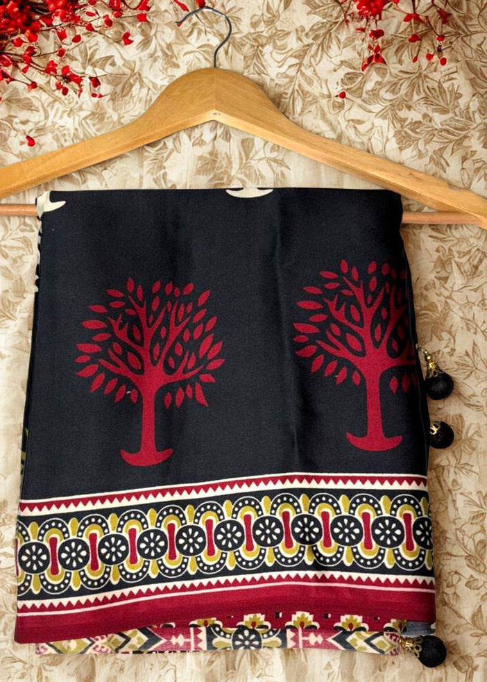 Black modal silk fabric Azrakh saree with red tree designs and colorful border on a wooden hanger against a floral background.